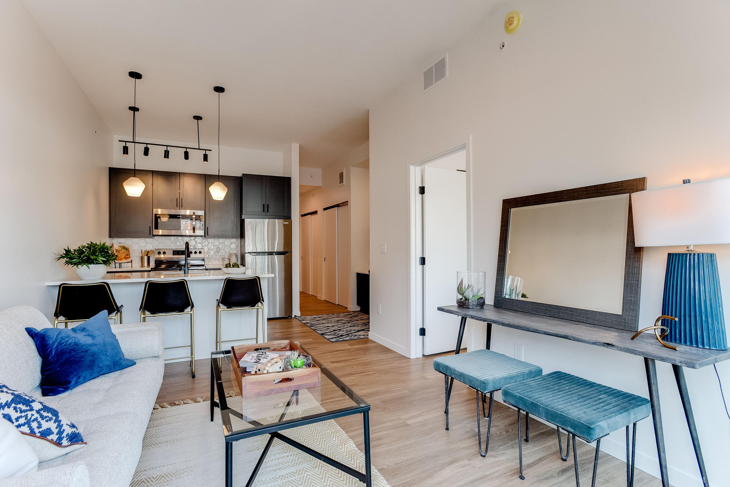 Modern apartment living room with a couch, blue accents, kitchen, and bar stools in the background.