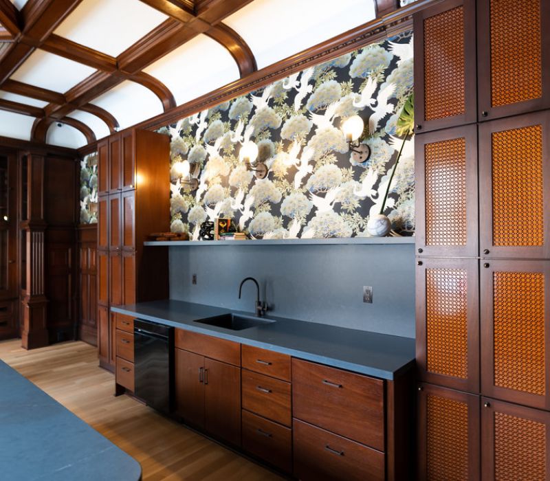 Kitchen with dark wood cabinets, black countertop, and floral wallpaper above the sink and backsplash.