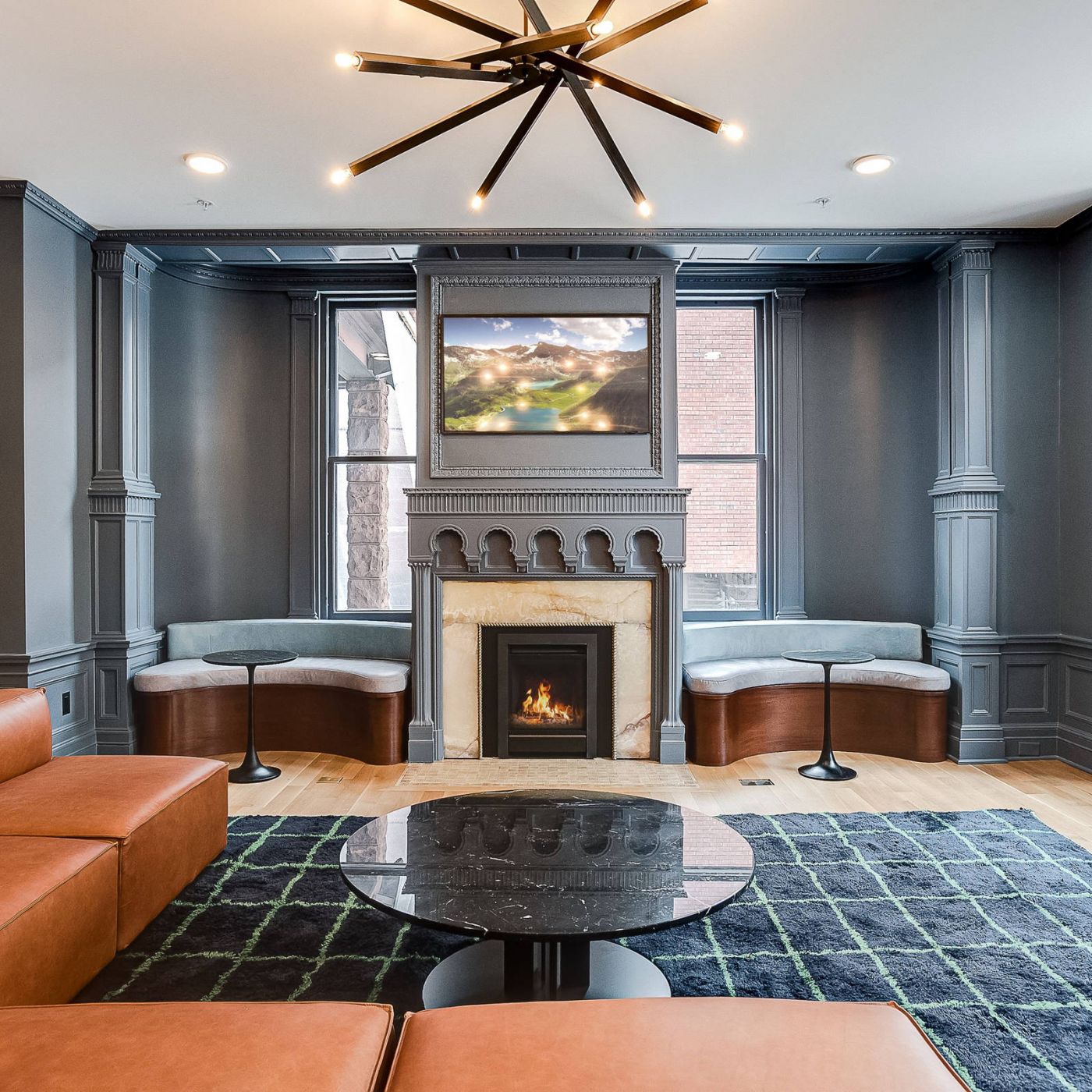 Modern living room with gray walls, brown leather sofa, fireplace, and large windows letting in natural light.