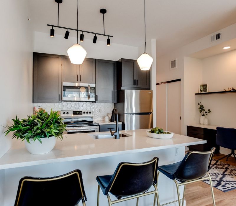 Modern kitchen with dark cabinets, stainless steel appliances, and a breakfast bar with three black chairs.