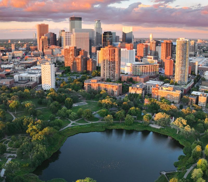 Aerial view of a city skyline at sunset with a pond and green park in the foreground.