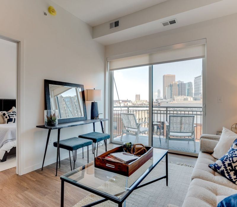 Modern living room with city view, balcony, cozy sofa, glass coffee table, and adjacent bedroom.