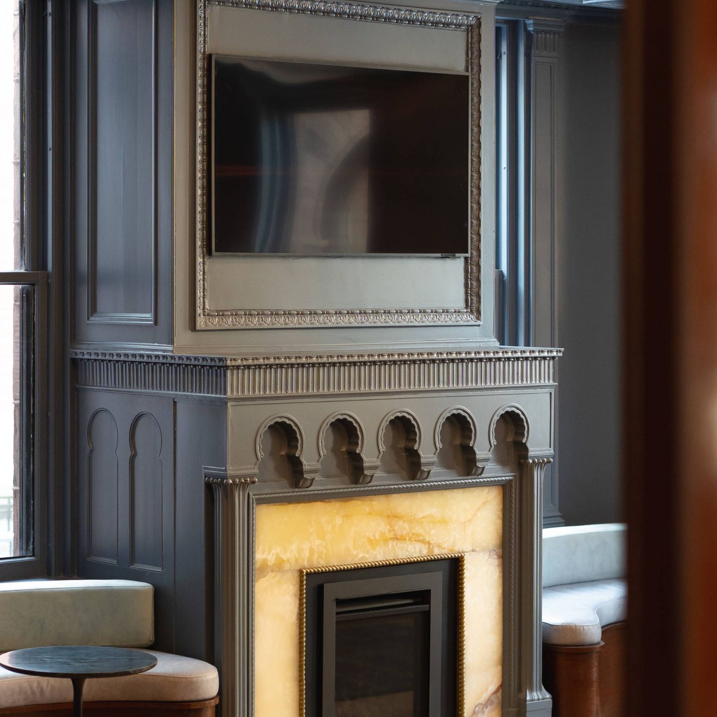 A modern fireplace with ornate trim, an onyx surround, and a large TV mounted above it in a stylish room.