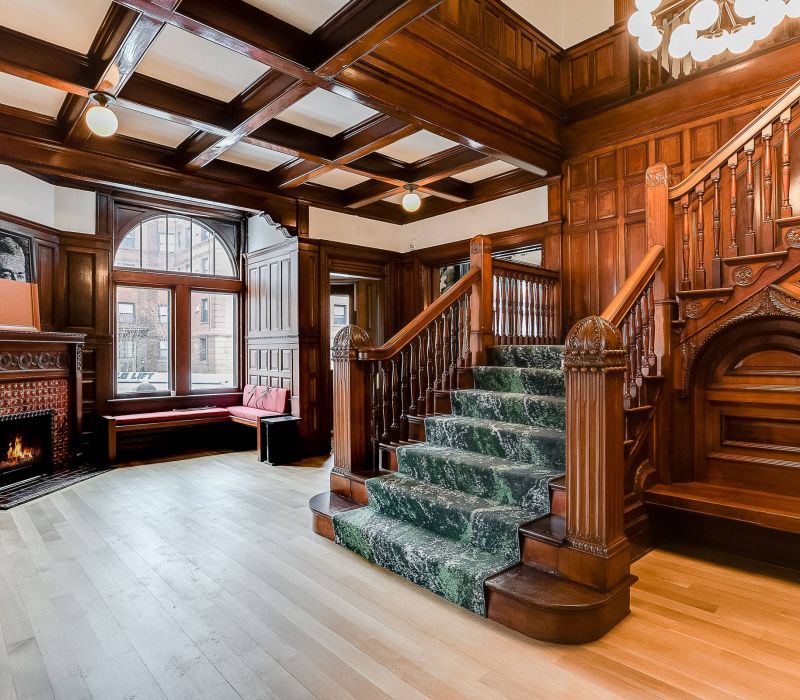 Grand wooden staircase, coffered ceiling, fireplace, and large windows with built-in bench in an elegant, historic room.
