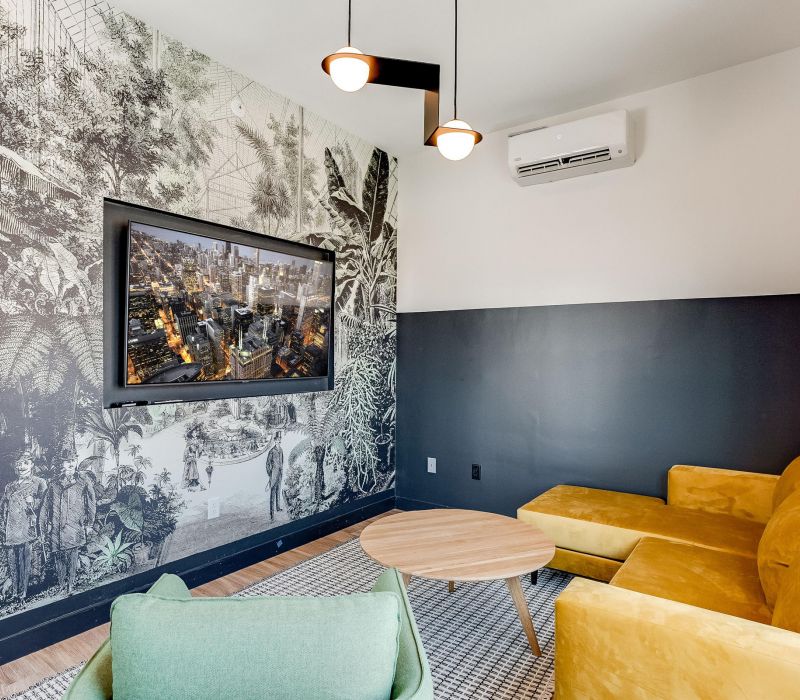 Cozy lounge with a yellow sofa, green chair, wall TV, and black-and-white botanical mural on the wall.