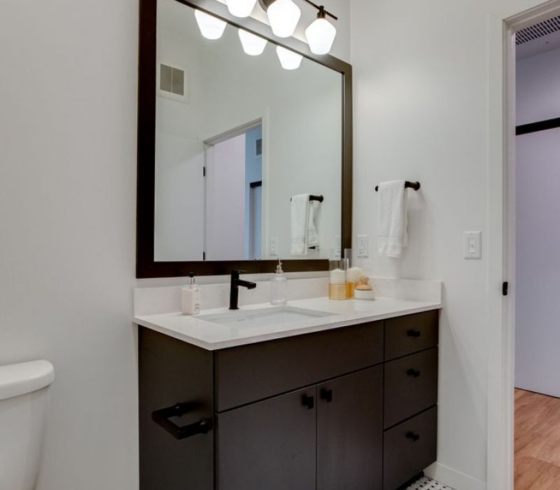 Modern bathroom with black vanity, large mirror, white countertop, and patterned tile floor.