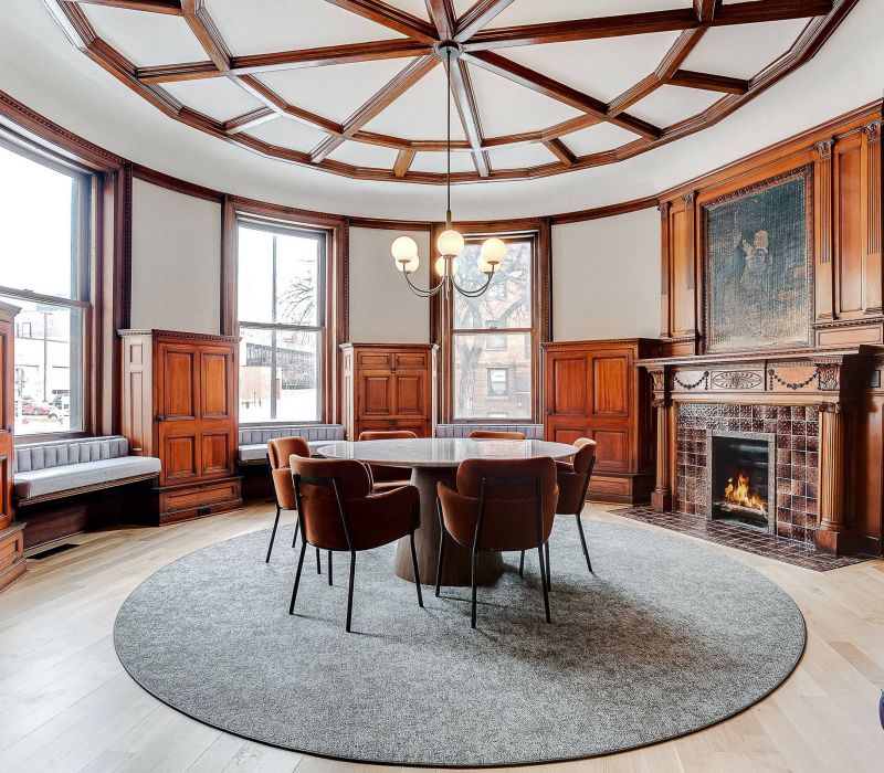 Round dining room with wood paneling, a fireplace, chandelier, and large windows providing natural light.