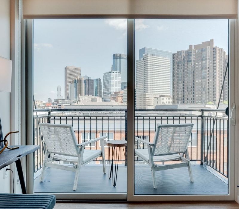 A city skyline view from a balcony with two white chairs and a small table.
