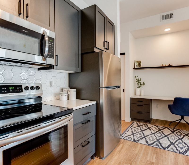 Modern kitchen with stainless steel appliances, hex tile backsplash, and a small home office nook in the background.